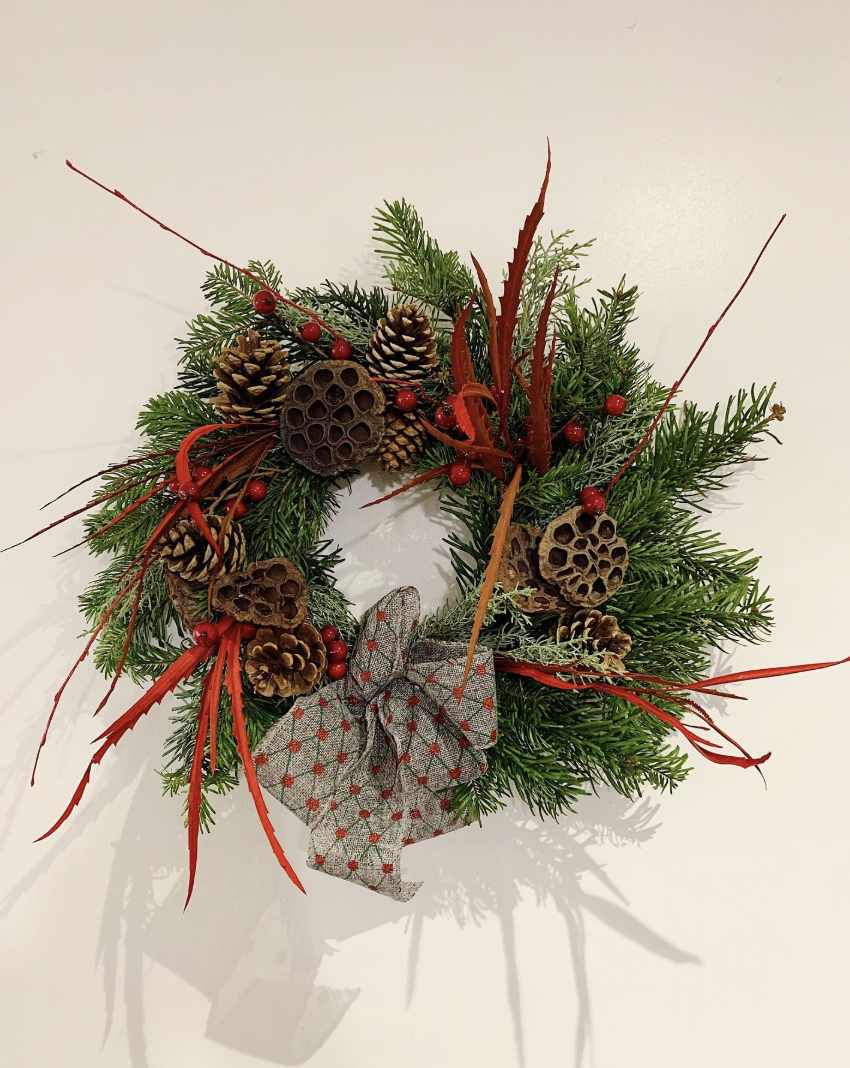 Handmade Christmas door wreath of fresh spruce with pine cones, lotus pods, red berries and a spotted hessian bow