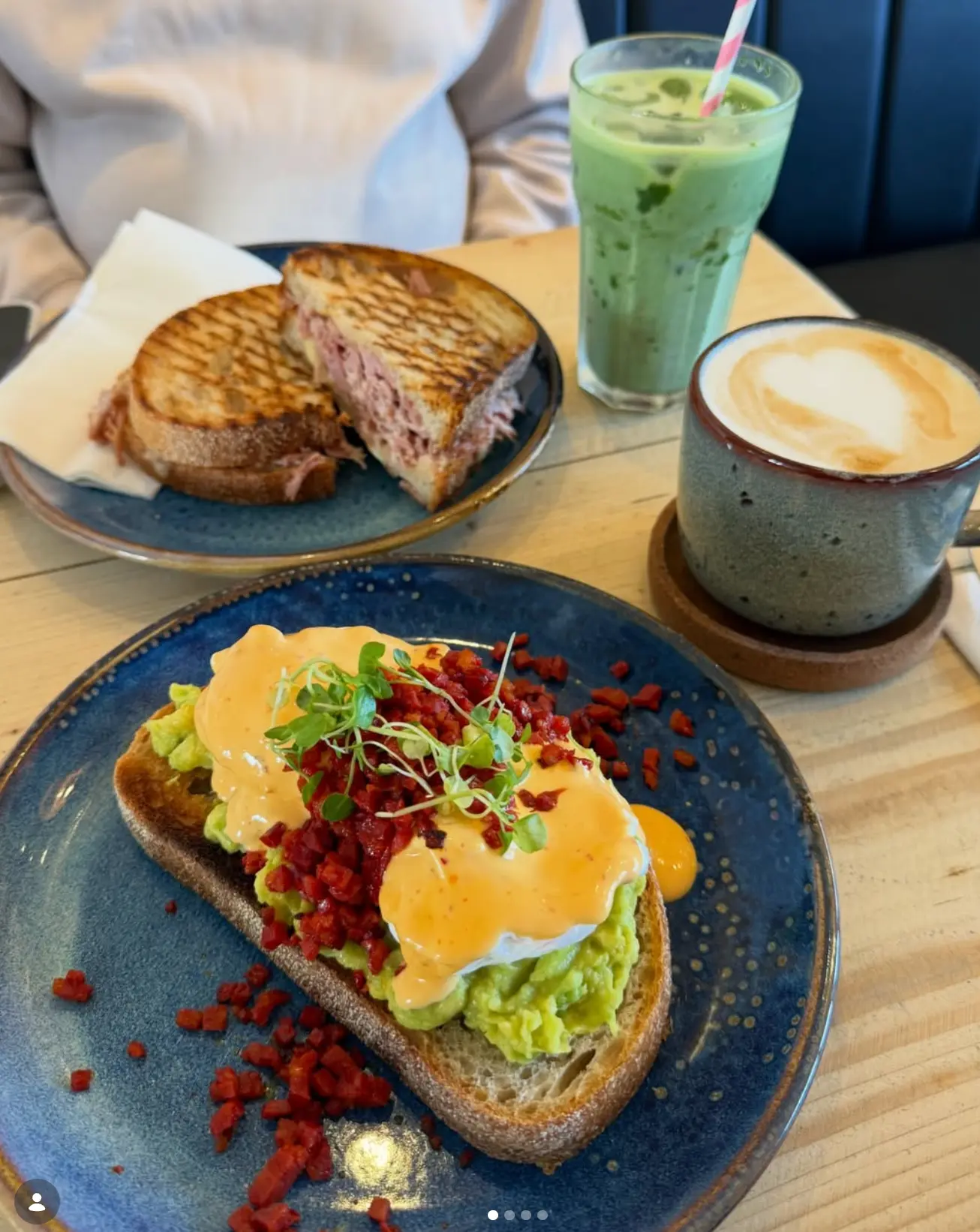 Eggs benedict on sourdough, a toasted ham sandwich and a flat white on a wooden table at Leaf + Bean