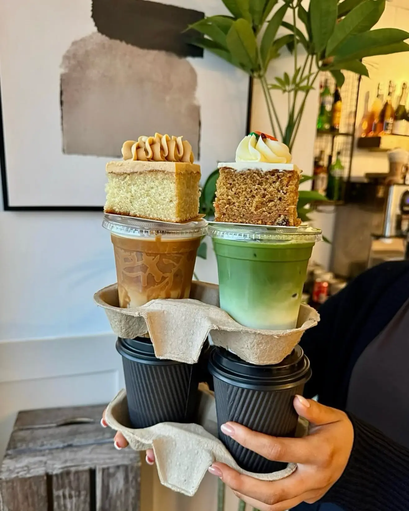 Slices of coffee cake and carrot cake balanced on takeaway drinks from Leaf + Bean