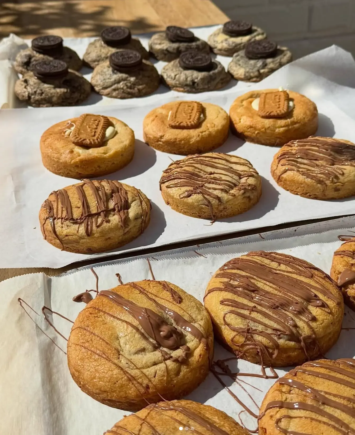 Trays of freshly baked Oreo, Biscoff and Nutella drizzle cookies cooling in the sun
