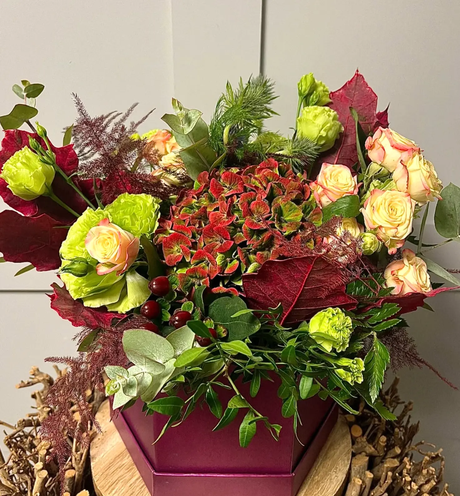 A hexagonal burgundy box filled with russet hydrangea, cream roses and lime carnations