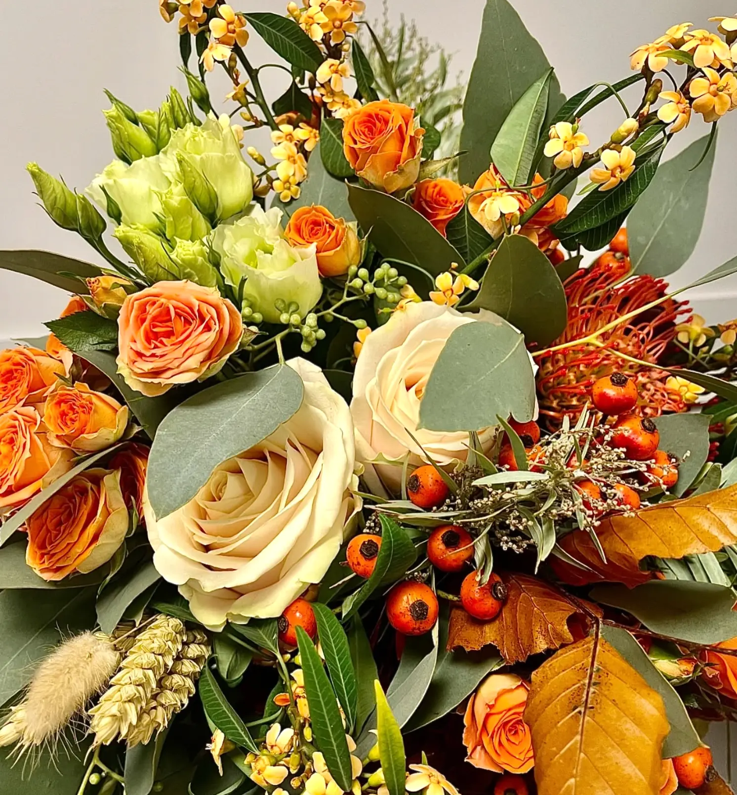 An autumn bouquet of cream and orange roses, protea, rose hips and copper beech leaves