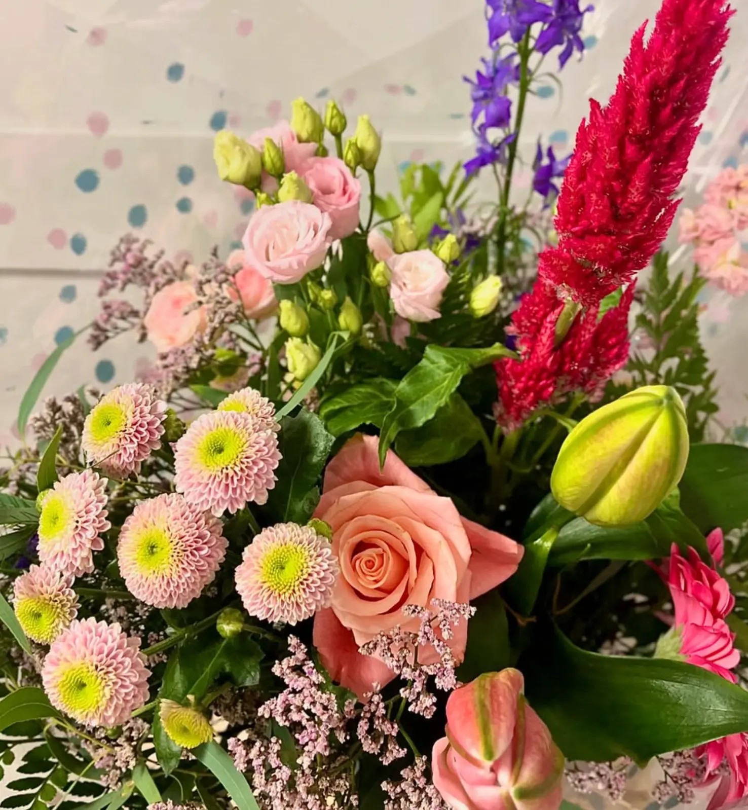 A pastel hand-tied bouquet of peach roses, pink chrysanthemums, celosia and delphinium