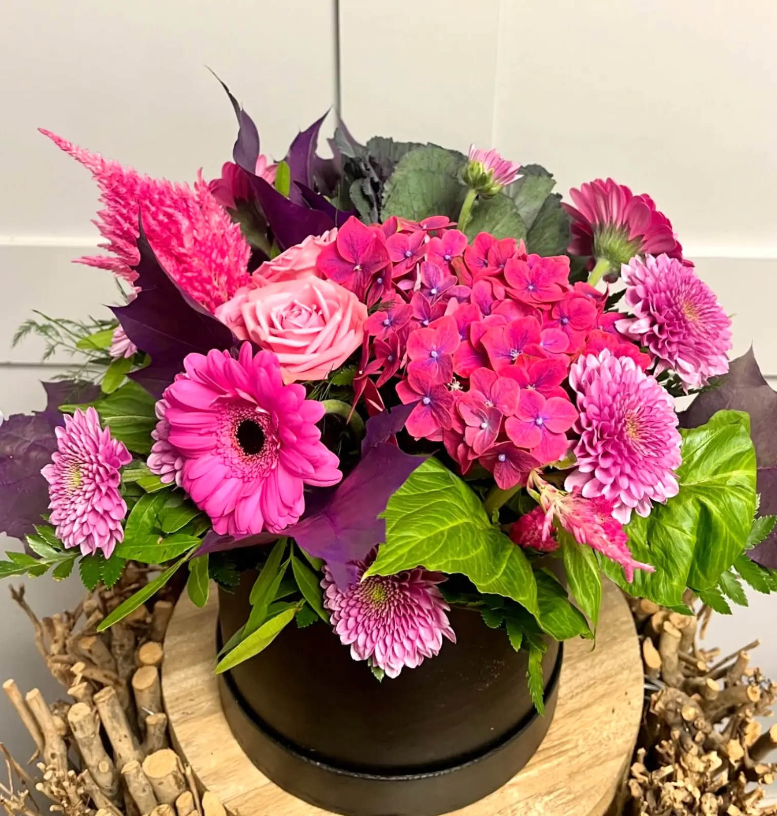 A bright pink hat box arrangement of hydrangea, gerbera and chrysanthemums