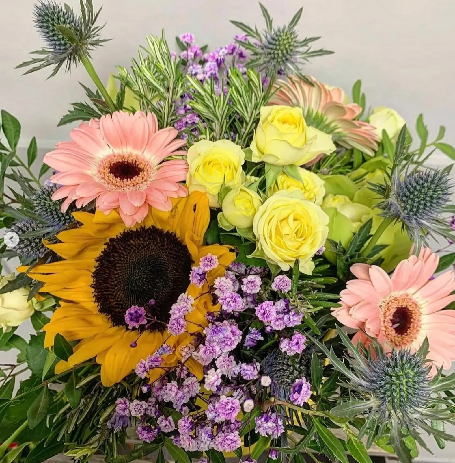 A summer bouquet with a sunflower, pink gerberas, yellow roses and purple statice