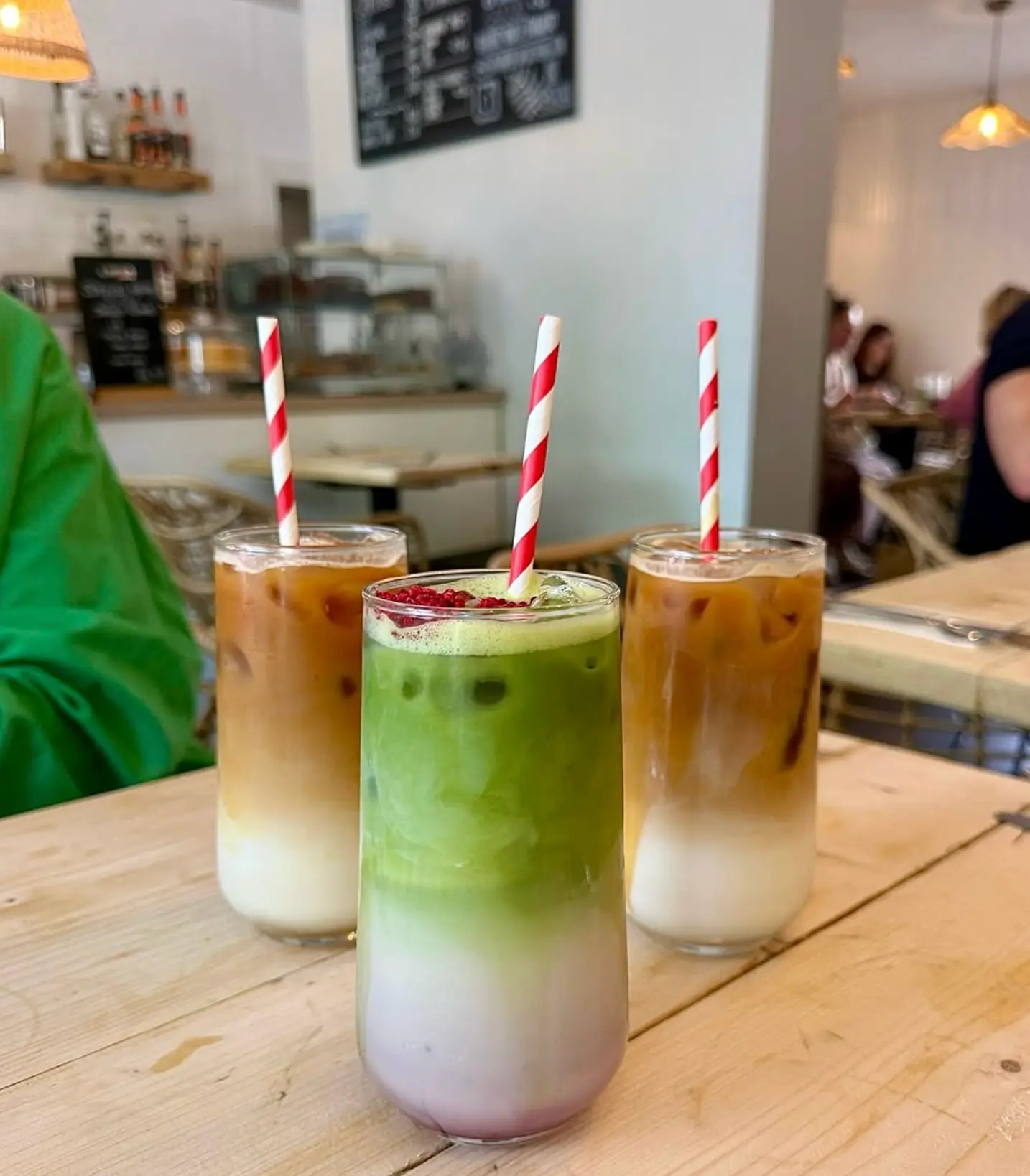 Iced coffee and layered iced matcha with red striped straws on a cafe table