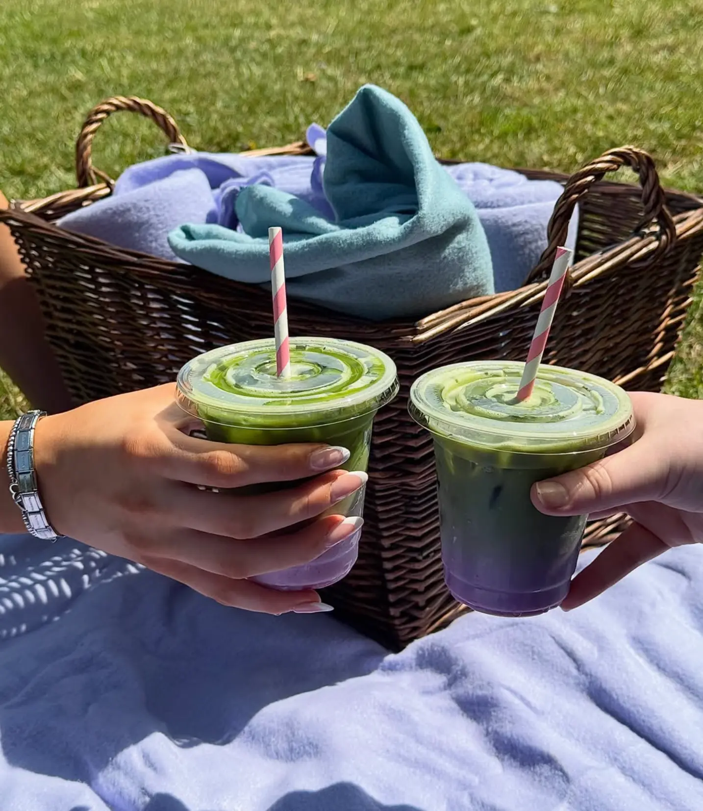 Two iced matcha lattes held over a picnic blanket