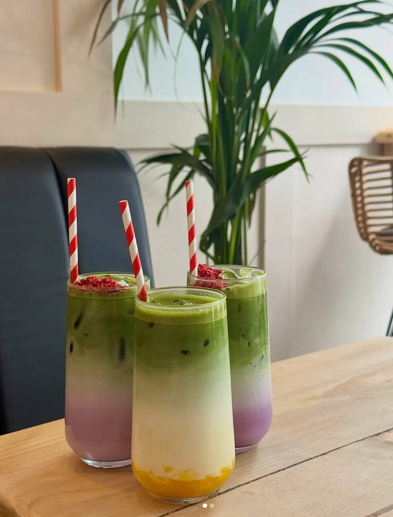 Three tall glasses of layered iced matcha with striped straws on a wooden table at Leaf + Bean
