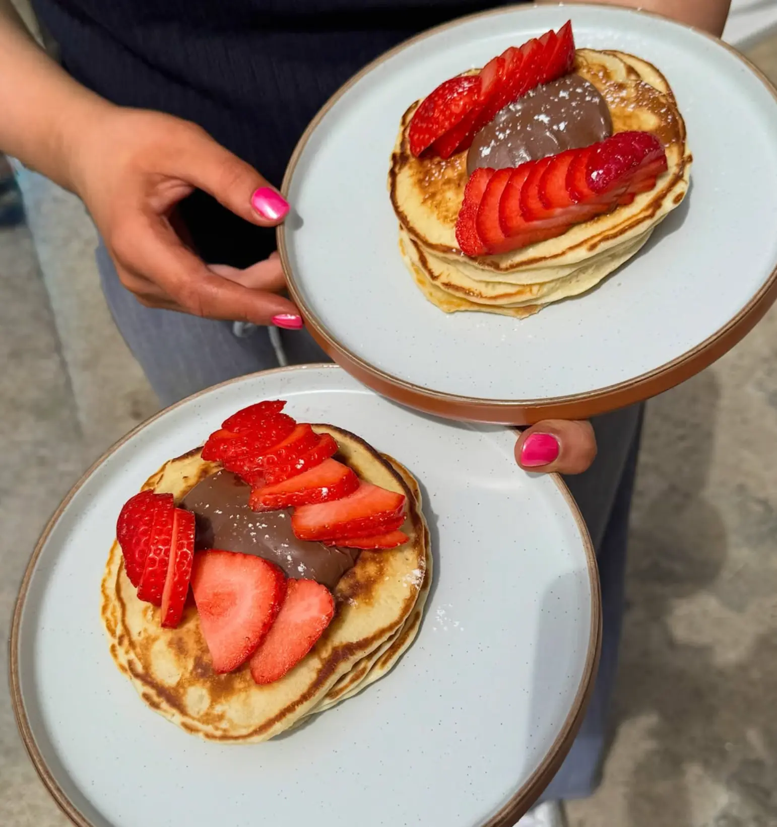 Two stacks of fluffy pancakes topped with chocolate spread and sliced strawberries