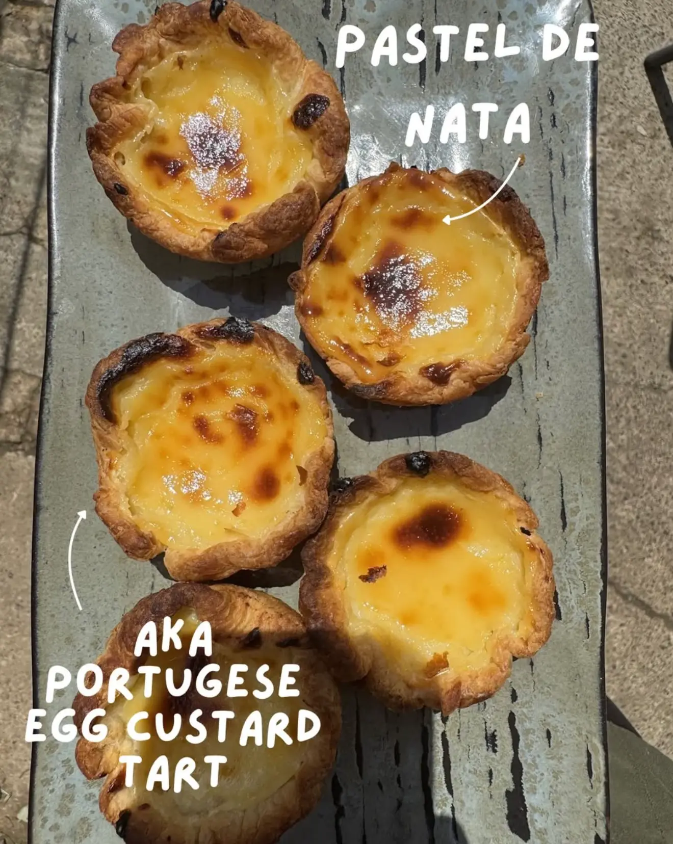 Five pastel de nata Portuguese custard tarts on a grey tray at Leaf + Bean