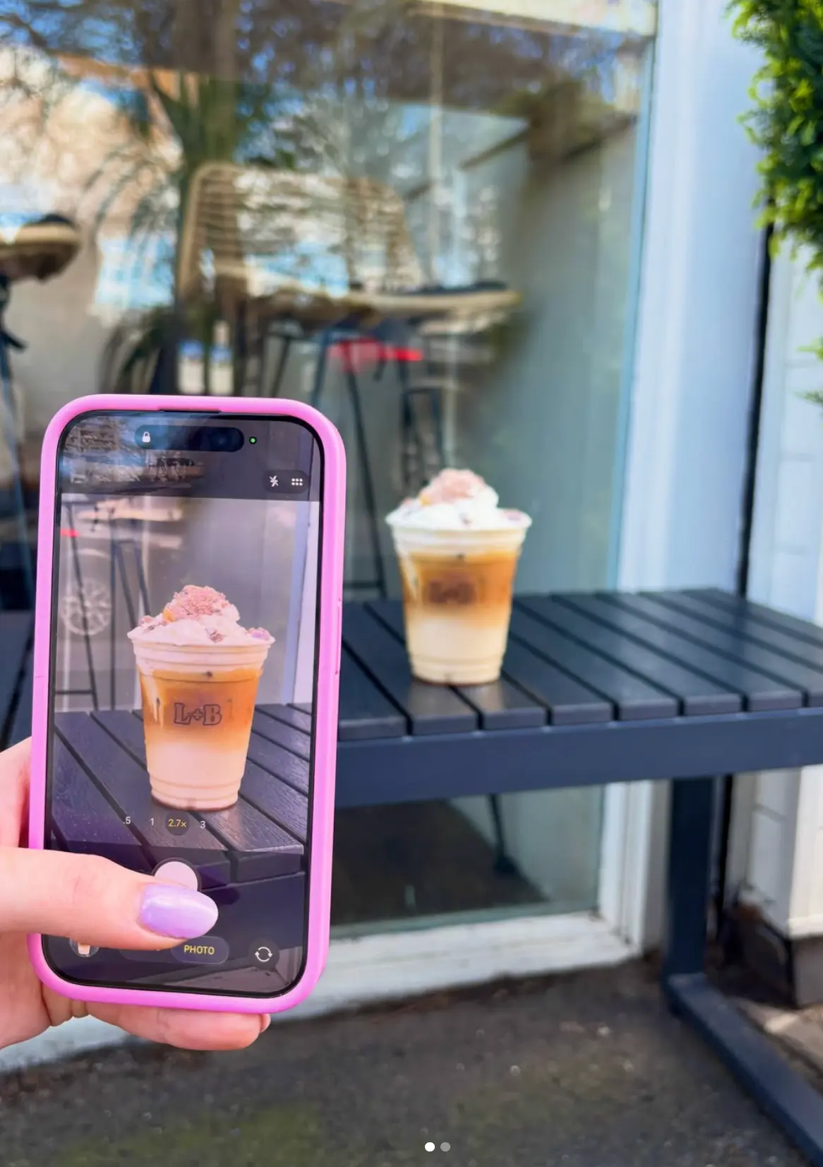 A customer photographing an iced coffee on a light wooden table at Leaf + Bean