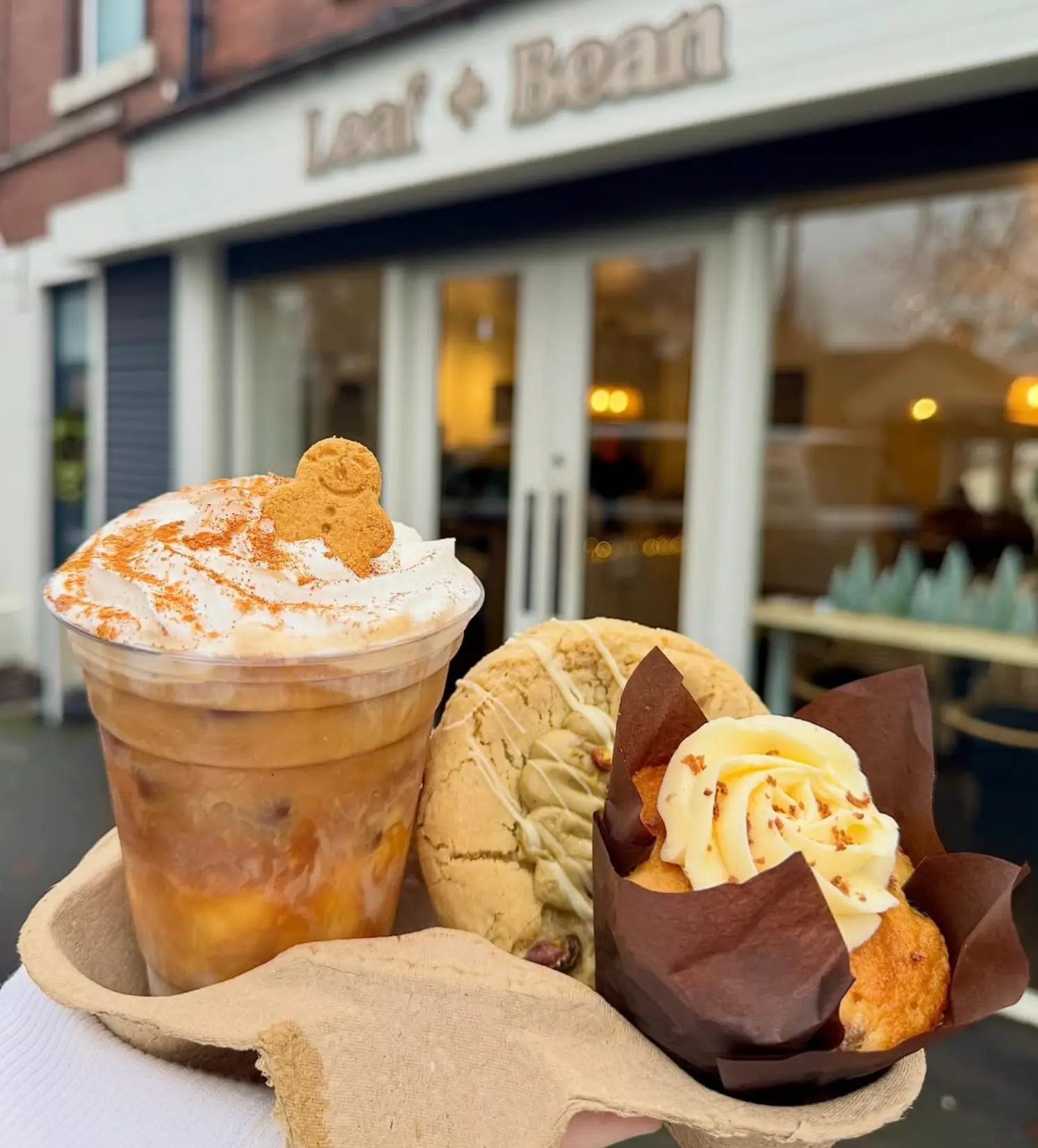 A gingerbread iced latte, cookie and muffin held outside the Leaf + Bean shopfront