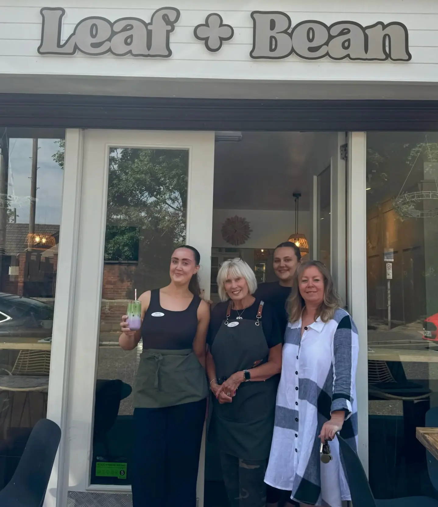 The four-strong Leaf + Bean team standing together in the cafe doorway beneath the shop sign